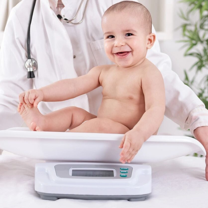 A baby is sitting on the scale while a doctor examines it.