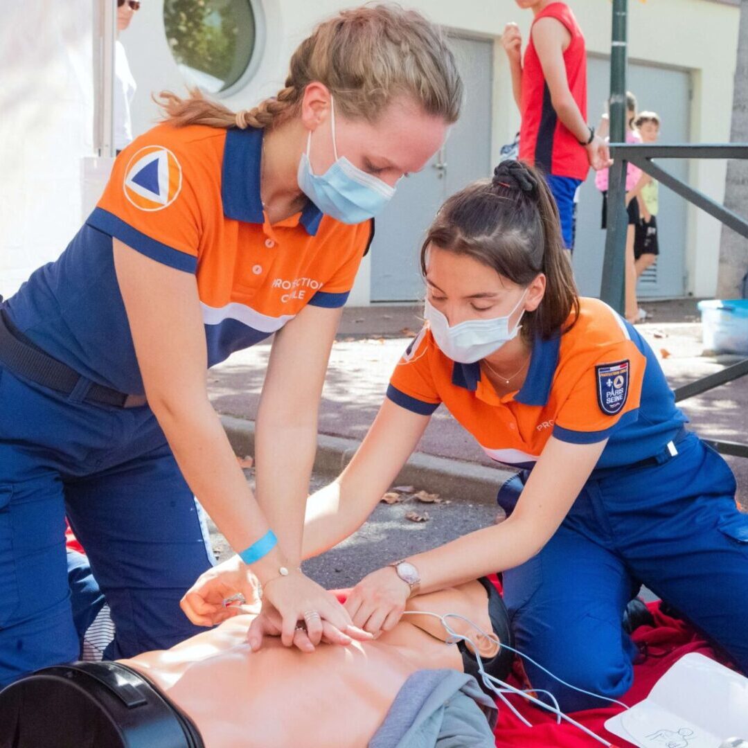 Two women in orange shirts are practicing cpr on a dummy.